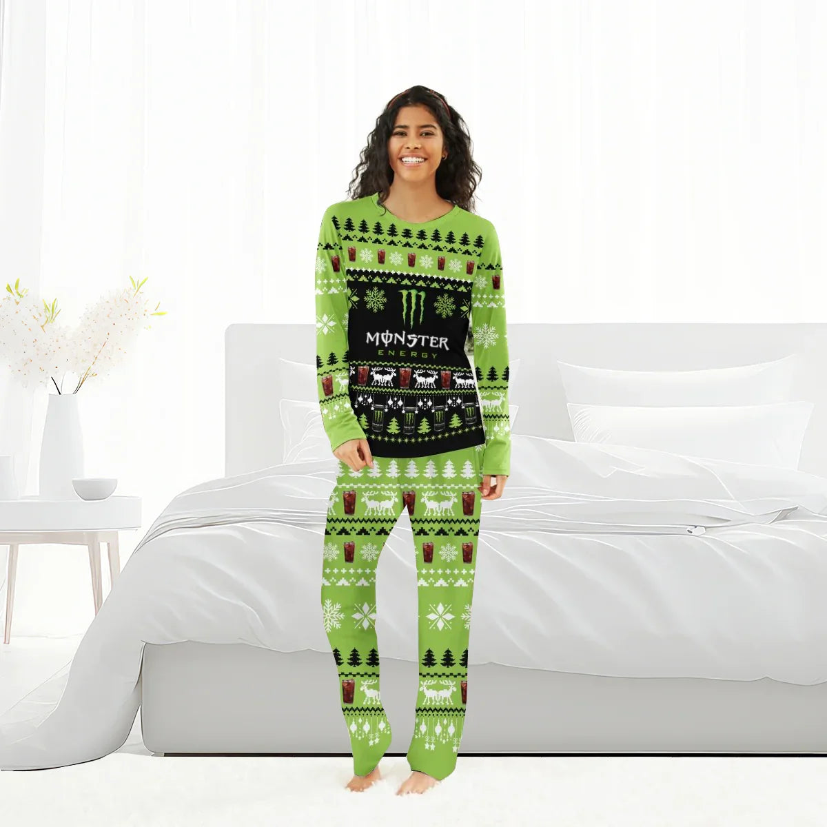 Smiling woman in green Monster Energy Christmas pajamas standing in a bright bedroom with white bed