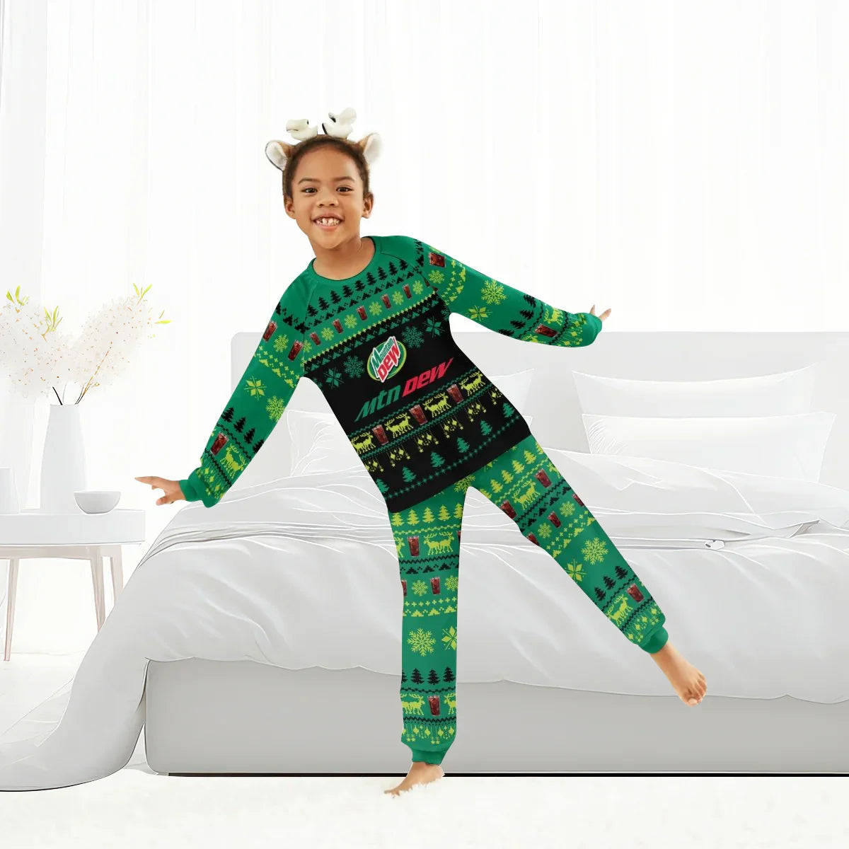 Child wearing green Mountain Dew Christmas pajama set with reindeer antler headband in white bedroom
