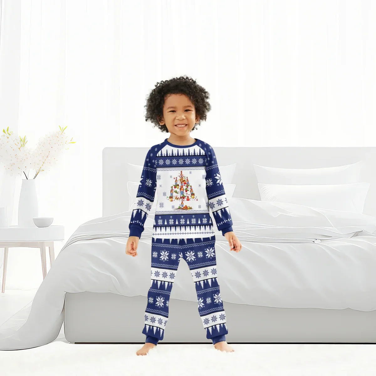Smiling child wearing blue and white Christmas pajamas with snowflakes and Christmas tree design in bright bedroom