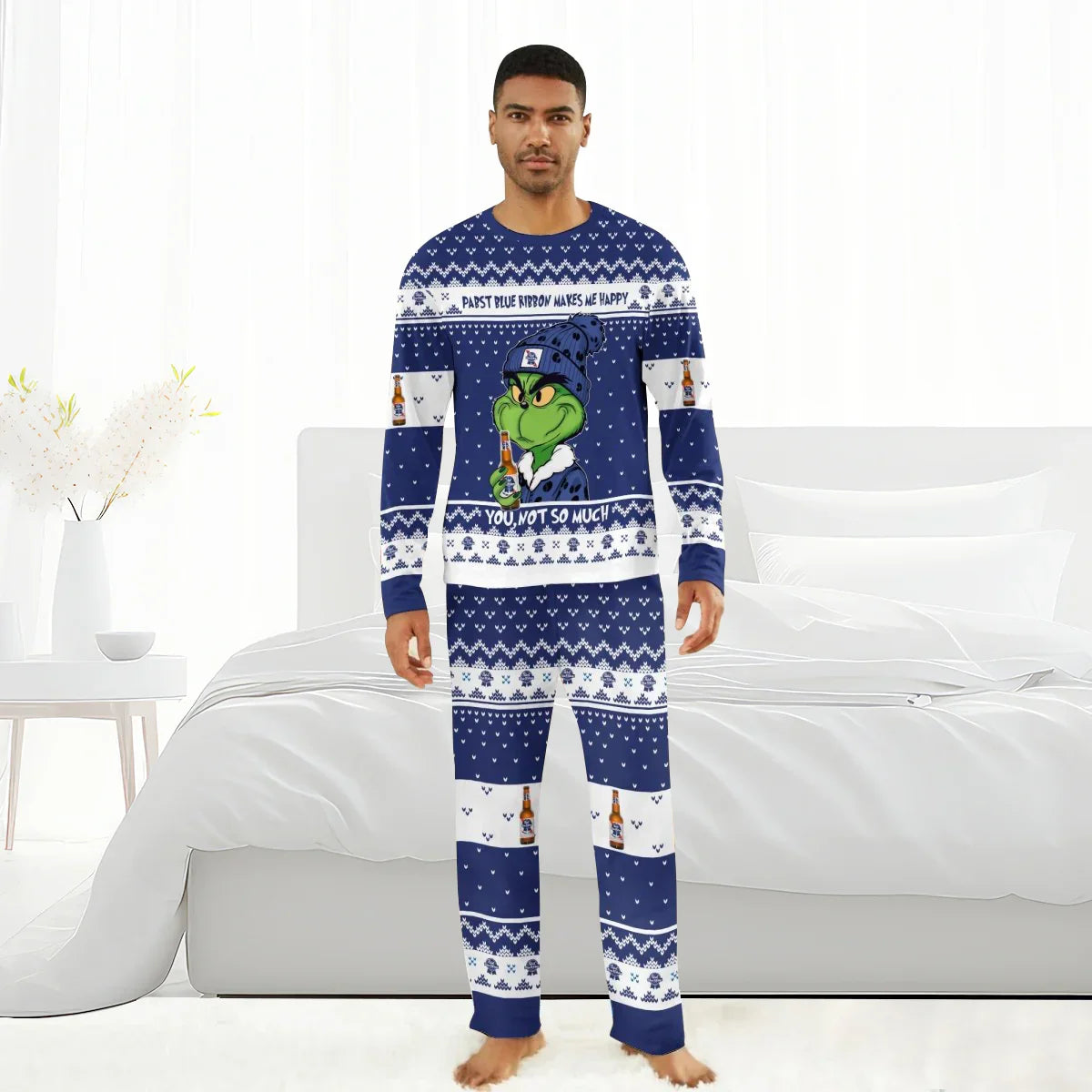Man wearing navy blue Grinch-themed Pabst Blue Ribbon holiday pajamas standing barefoot in white bedroom