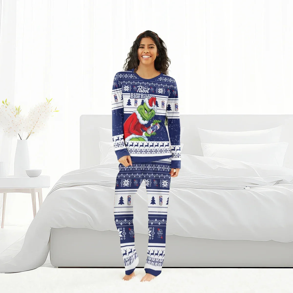 Smiling woman in navy Blue Ribbon Grinch Christmas pajamas standing in bright white bedroom