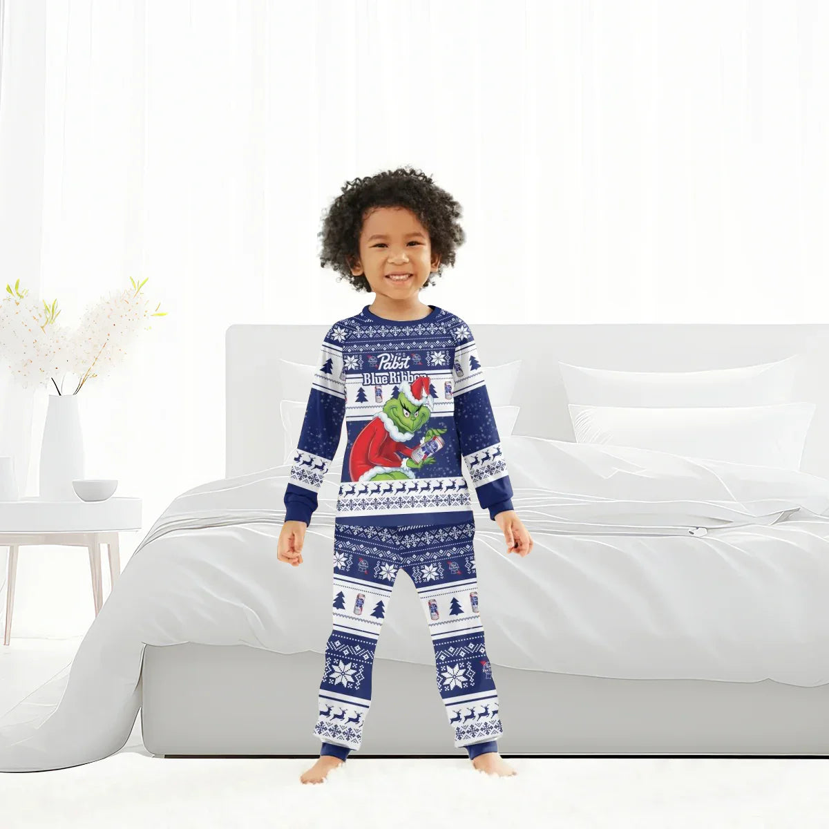 Child wearing blue Pabst Blue Ribbon Grinch holiday pajamas standing in a bright bedroom with white bed and decor