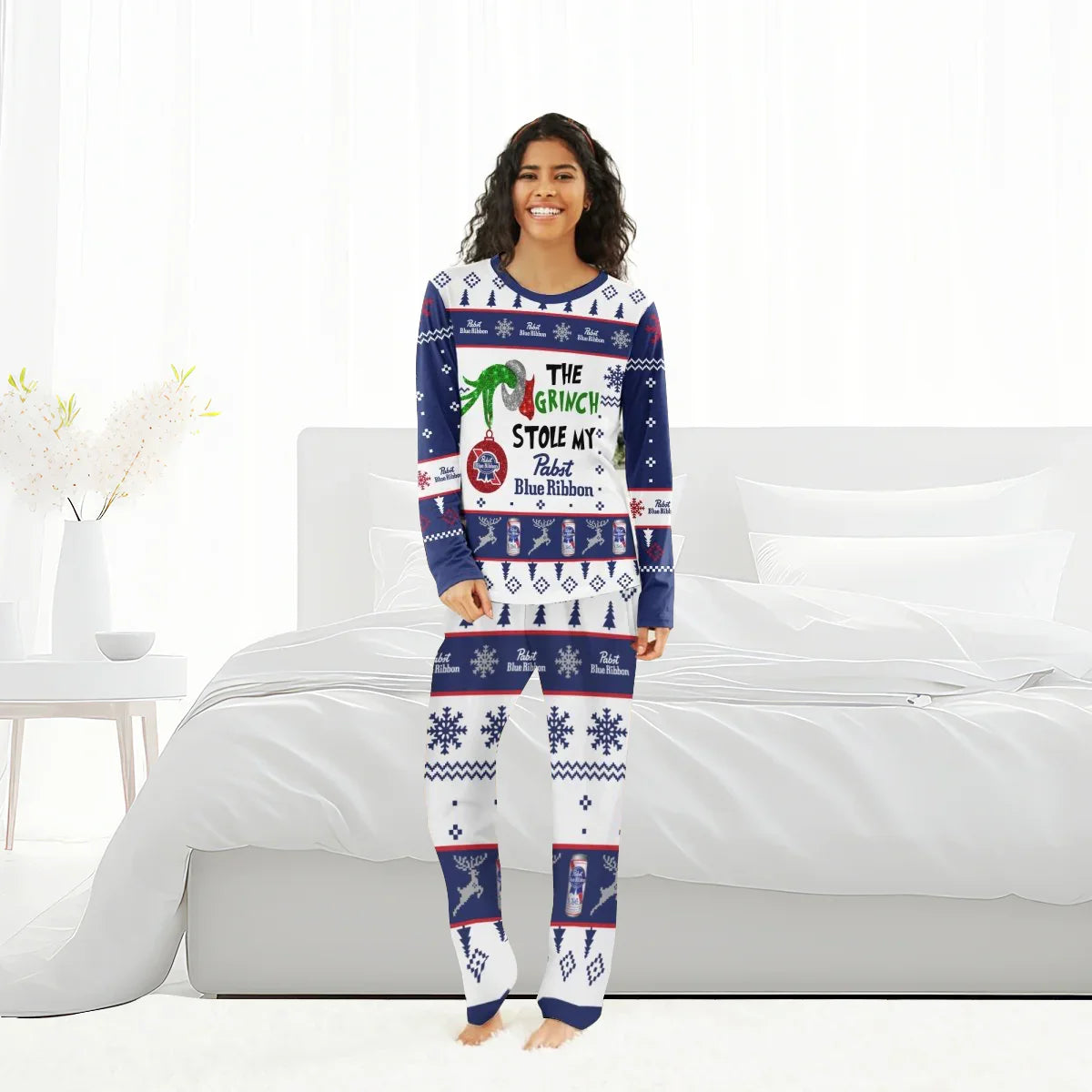 Smiling woman in festive The Grinch stole my Pabst Blue Ribbon holiday pajamas standing in white bedroom