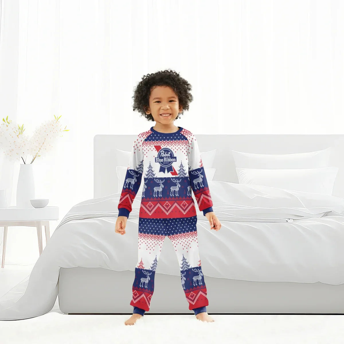 Smiling child in red, white, and blue Pabst Blue Ribbon reindeer pajama set standing in a bright modern bedroom