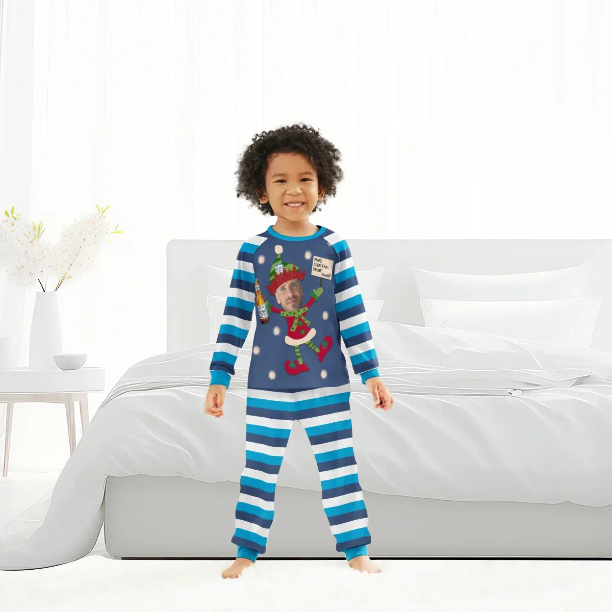 Smiling child in blue striped personalized Christmas pajamas with elf and beer bottle design standing in a bright bedroom