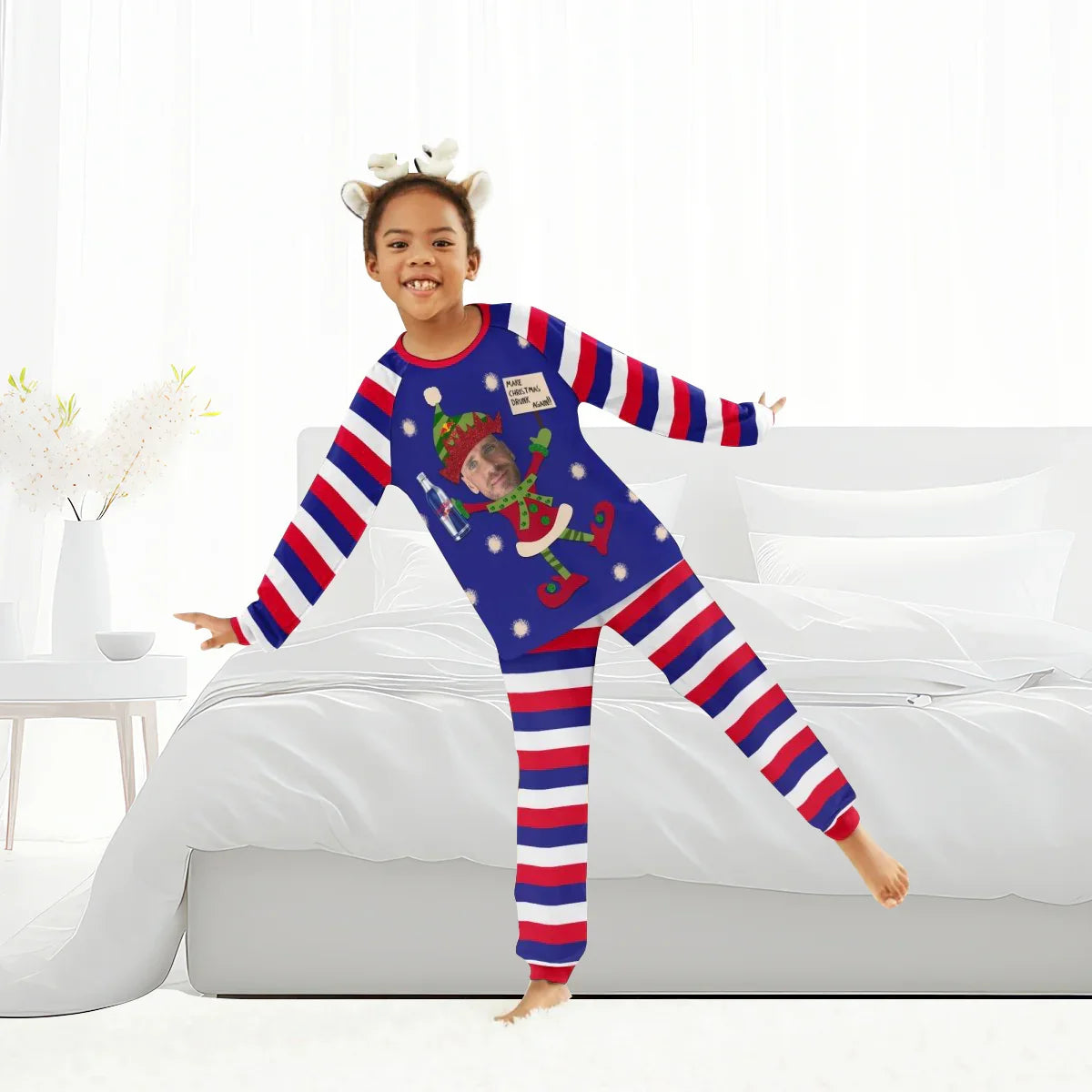 Smiling child in festive red, white, and blue striped Christmas pajamas with personalized elf design and reindeer headband