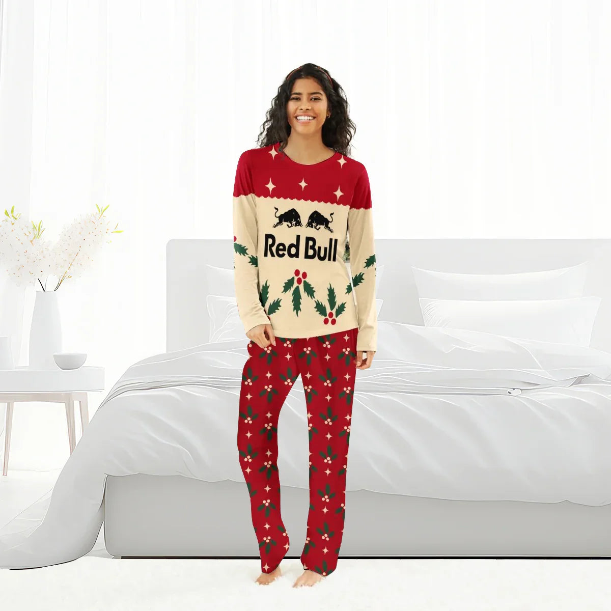 Smiling woman in Red Bull Christmas pajamas with red, beige, and holly leaf design in white bedroom
