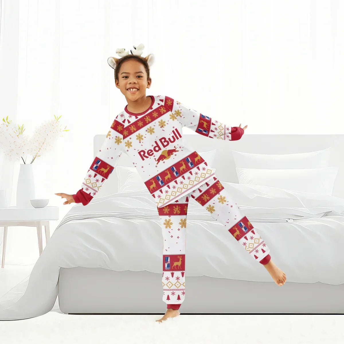 Girl wearing Red Bull holiday pajamas with reindeer and snowflake patterns standing by white bed