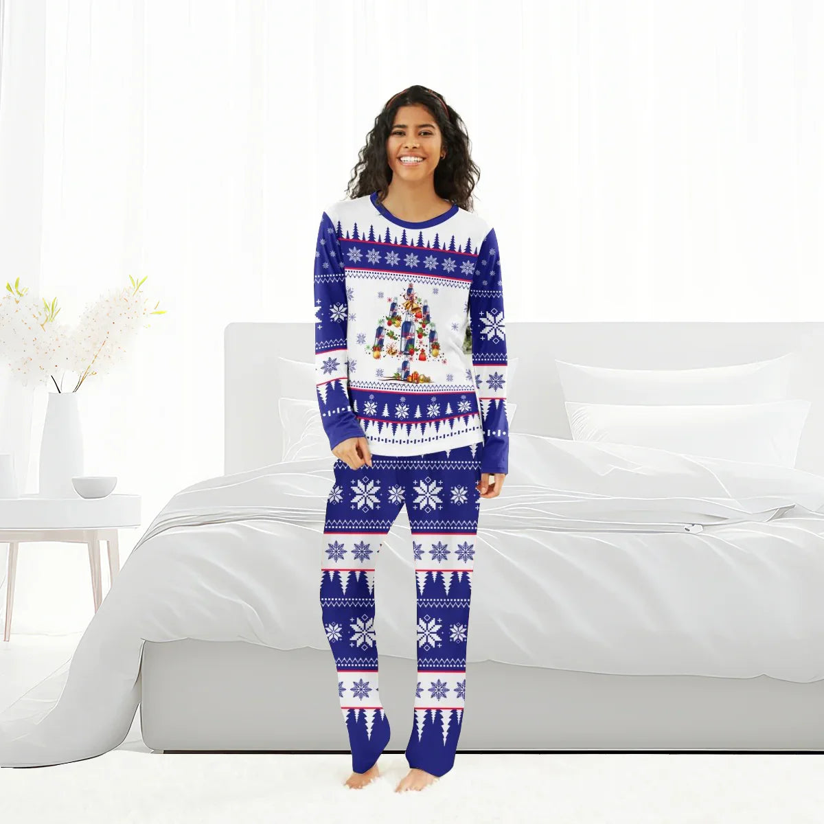 Smiling woman in blue and white Christmas tree-themed holiday pajamas standing in bright white bedroom
