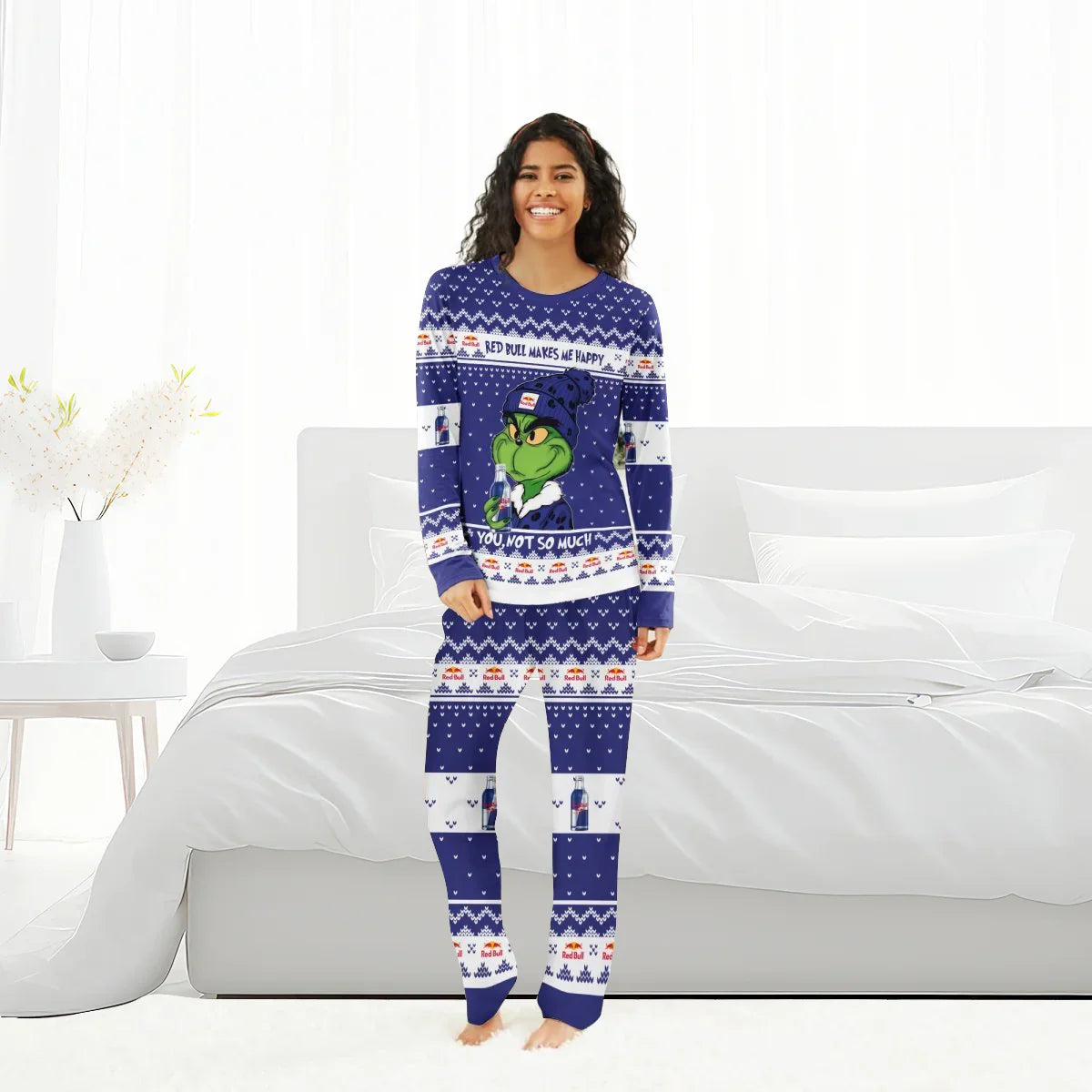 Smiling woman in blue Red Bull Grinch holiday pajamas standing barefoot in white bedroom