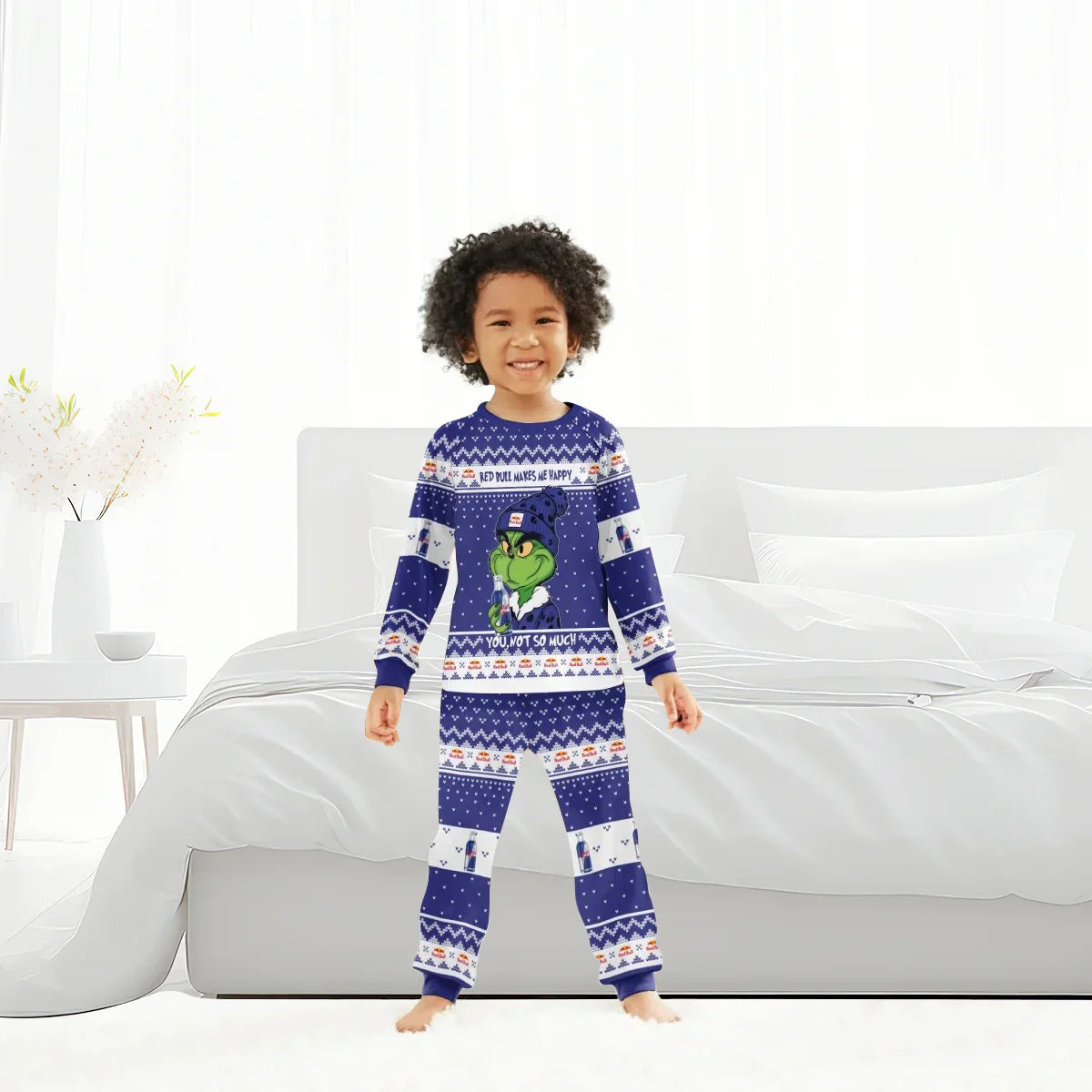 Smiling child wearing blue Grinch-themed Red Bull printed pajamas standing in modern white bedroom
