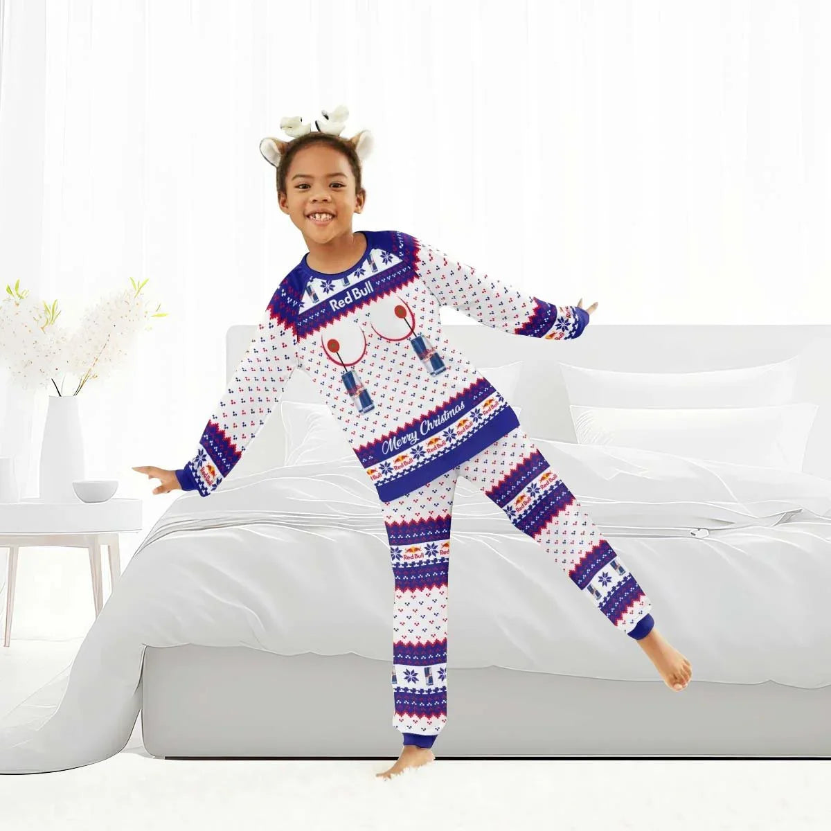 Happy child wearing Red Bull Merry Christmas holiday pajamas in white blue red, standing on bed in bright bedroom