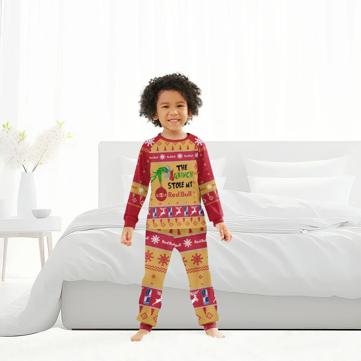 Smiling child in red and gold Christmas pajamas with Grinch and Red Bull holiday design, standing in bright bedroom