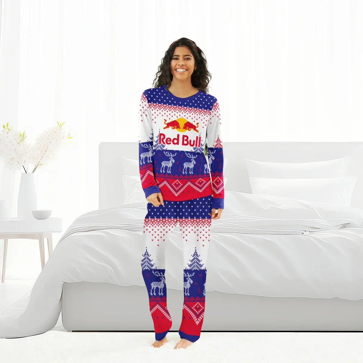 Smiling woman wearing Red Bull winter reindeer family pajamas in blue, red, and white, standing in bright bedroom