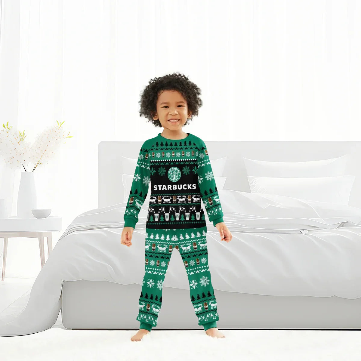 Smiling child in green Starbucks-themed Christmas pajamas standing barefoot in a bright white bedroom