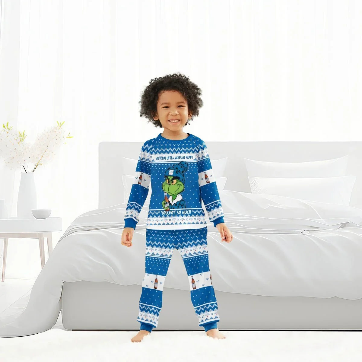 Smiling child in blue Grinch-themed holiday pajamas with Michelob Ultra beer design in bedroom