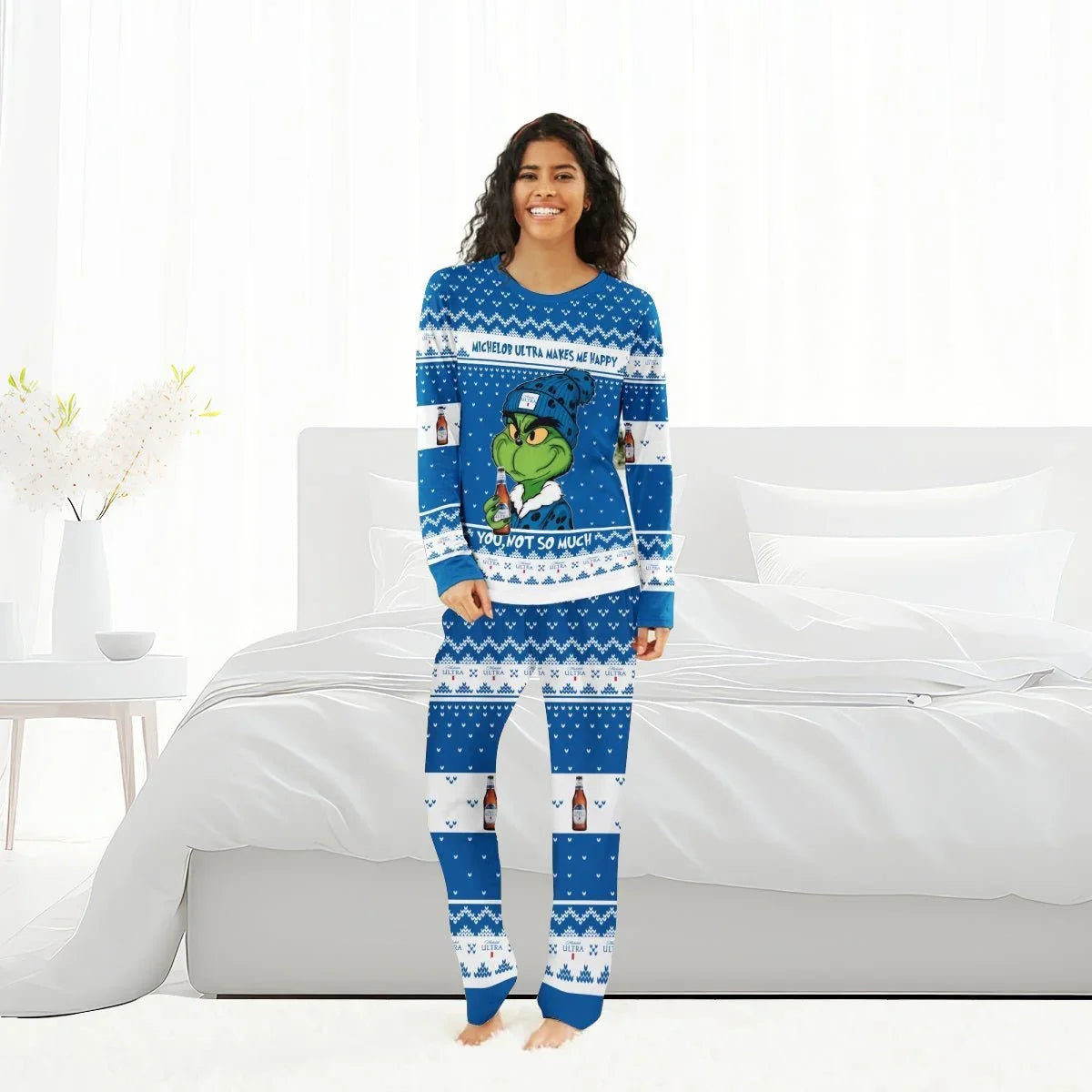 Smiling woman in blue Grinch-themed Michelob Ultra holiday pajamas standing in a bright bedroom